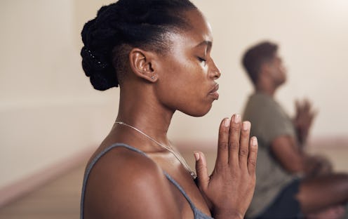 A person folds her hands in front of her chest with her eyes closed during yoga class. Yoga and Pila...
