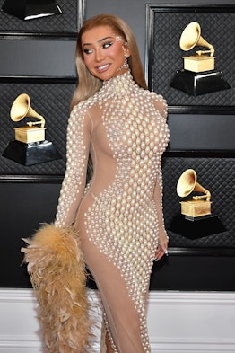 Nikita Dragun holds a feather boa and strikes a pose in a sheer embellished gown on the 2020 Grammys...