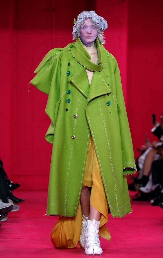 A model in a long olive coat, orange skirt and white trainers as a Spring 2020 trend from the coutur...