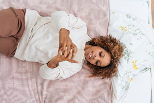 A woman uses her phone in bed first thing in the morning. Blue light's effects on sleep are variabl...