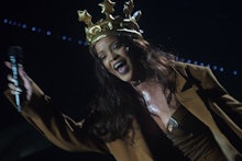 Rihanna with a crown holding the microphone towards the audience during a show