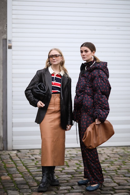 A woman in a red-white-black shirt, black blazer, and camel skirt, and a woman in a puffer suit at t...