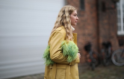 A blonde woman in a yellow coat a green feather bag at the Copenhagen Fashion Week