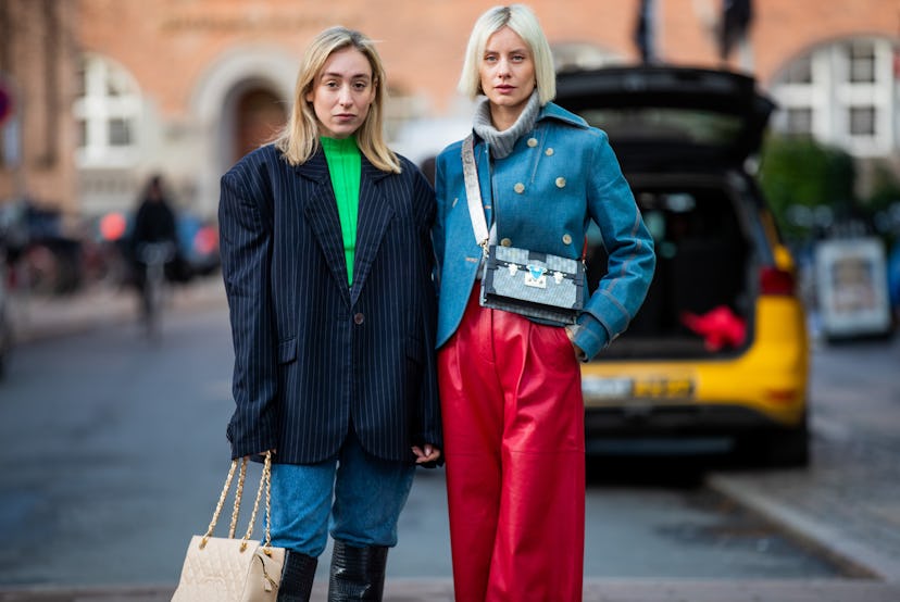 A woman in a green shirt navy blazer and denim jeans, and a woman in a blue jacket and red pants at ...
