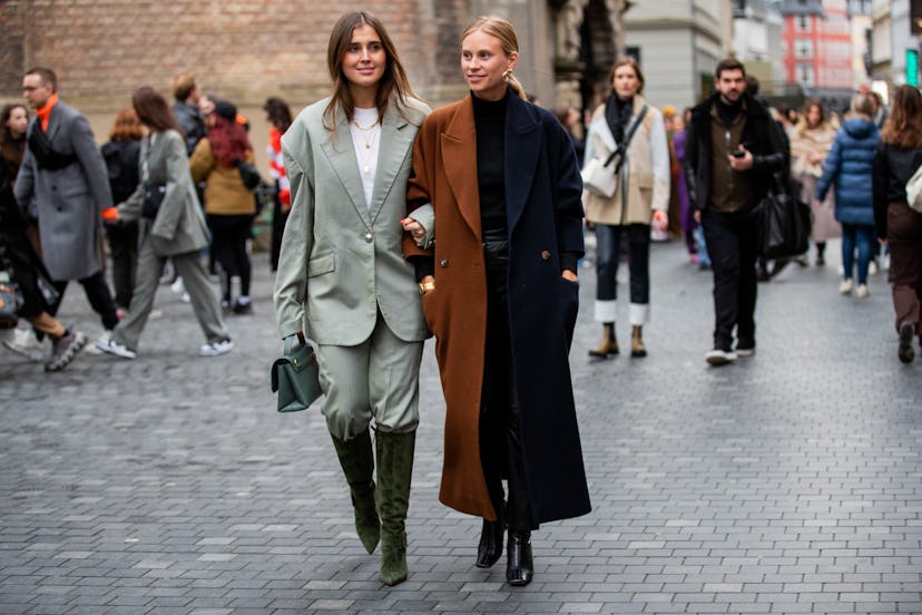 A woman in a grey suit and dark grey boots and a woman in a black-brown color-block coat at the Cope...