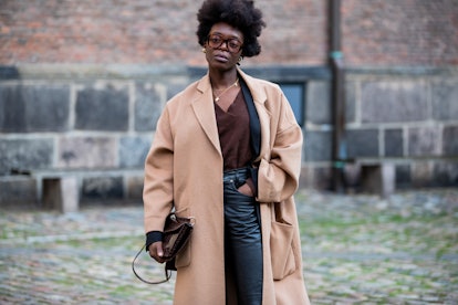 A woman in a brown sweater, camel coat, denim jeans and a brown bag at the Copenhagen Fashion Week