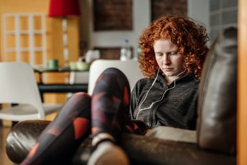 A young woman with curly red hair sitting on a couch while listening to a motivational podcast.