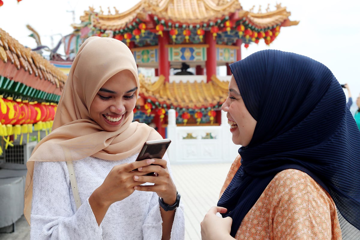 Two friends laugh and play on a phone while at a colorful temple on the Lunar New Year.