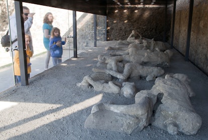 A family observing preserved bodies of Pompeii victims at 'The Garden of the Fugitives' in Italy.
