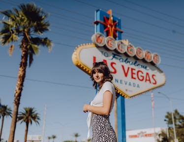 A young woman stands in front of the "Welcome To Fabulous Las Vegas" sign while on a summery trip.