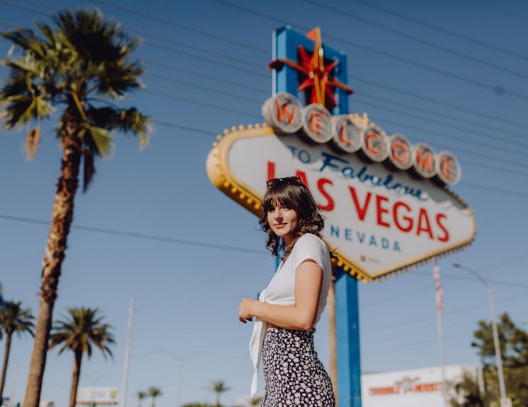 A young woman stands in front of the "Welcome To Fabulous Las Vegas" sign while on a summery trip.