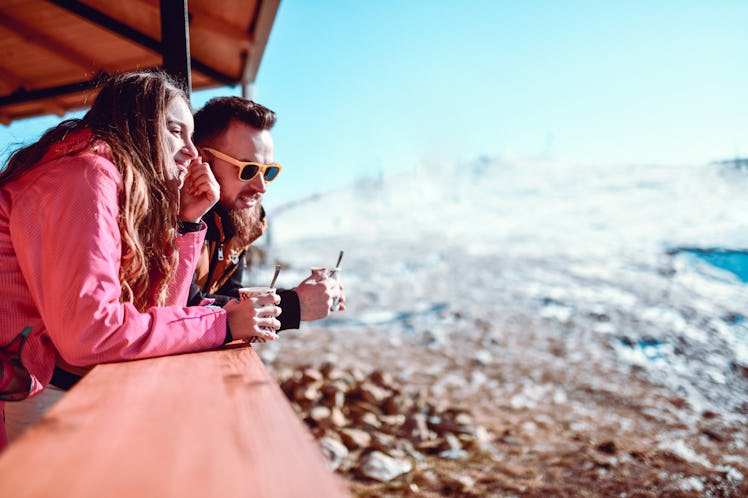 A couple enjoys cups of hot chocolate while on a romantic ski trip.