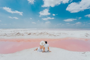 A couple shares a romantic moment on a pink beach while on a 25th birthday trip.