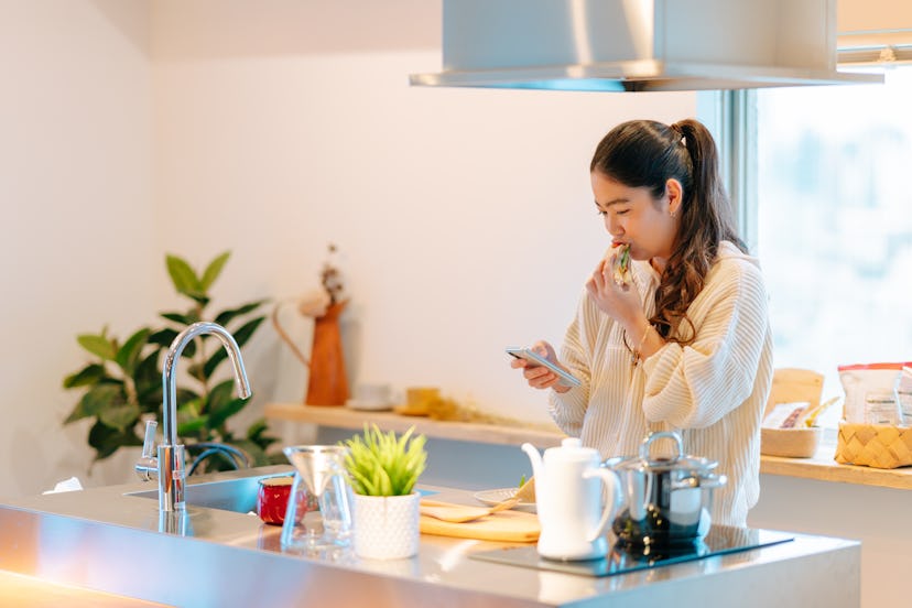 A woman eats vegetables while looking at her phone, where she's gotten an alarm reminder. Setting an...