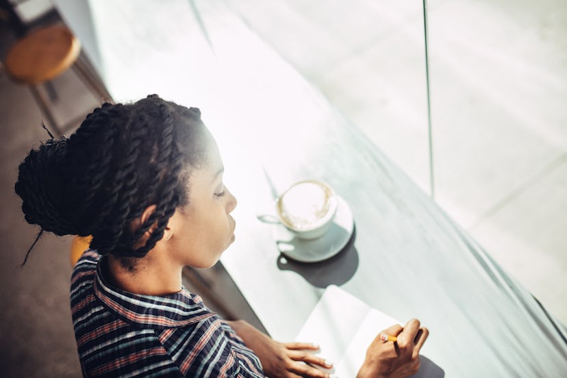 A woman journals in a sunlit café. Journaling is one key self-care practice for 2020.