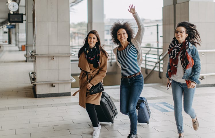 Three friends run through an airport with their suitcases because they're running late.