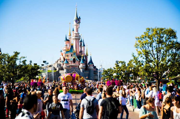 Crowds of people gather around Cinderella's castle in Disneyland Paris on a sunny day.