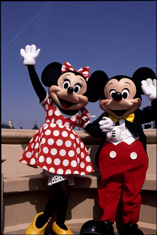 Minnie and Mickey Mouse wave to the camera while posing in Disneyland Paris.