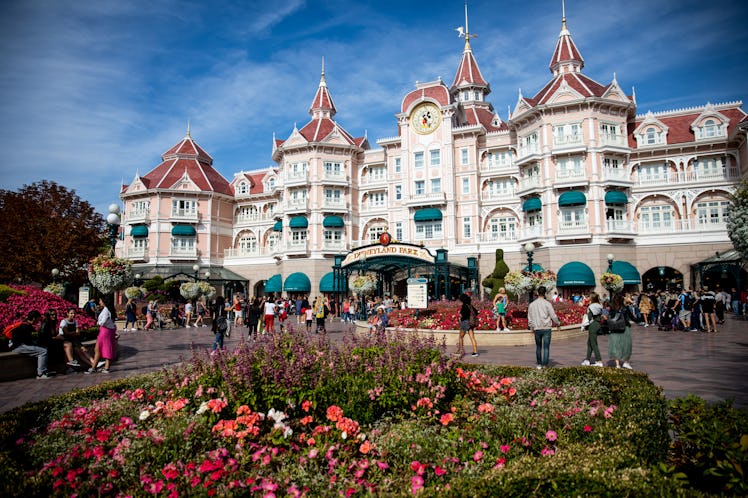 The main entrance to Disneyland Paris is decorated with flowers on a sunny, bustling day.
