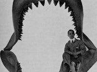 An old photograph of a man posing inside of the remains of a Megalodon's jaws