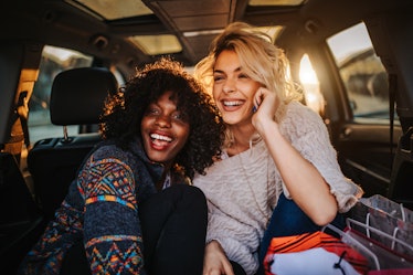 Two young women laugh while sitting in the trunk of a car at golden hour during a fall staycation.