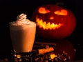 A latte drink sits in front of a jack-o-lantern for Halloween. 