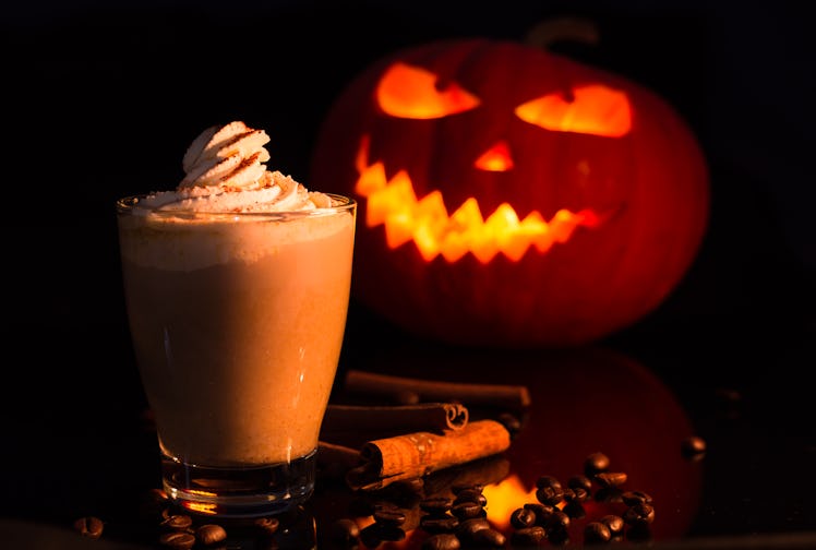 A latte drink sits in front of a jack-o-lantern for Halloween.
