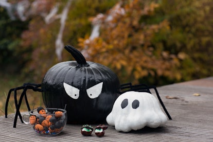 Two painted pumpkins, that have been crafted to look like a spider and ghost, sit on a wooden table ...