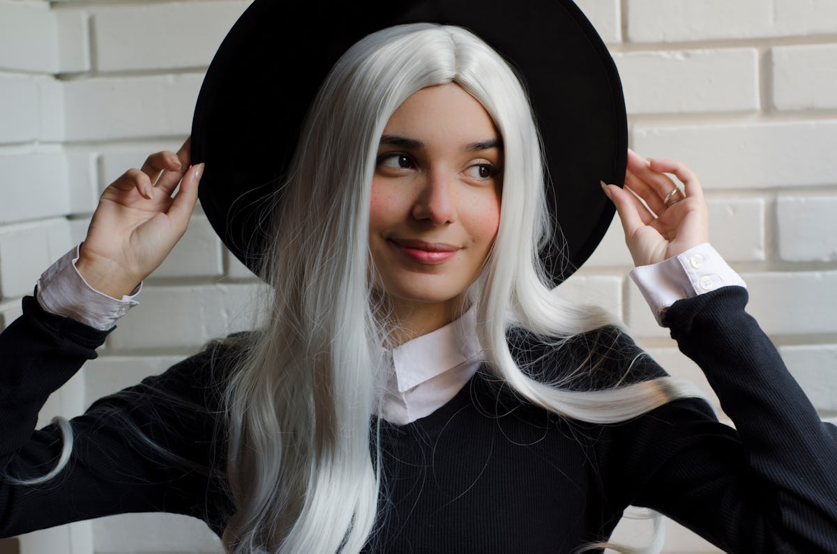 A woman with a long white wig poses in her witch hat for Halloween.