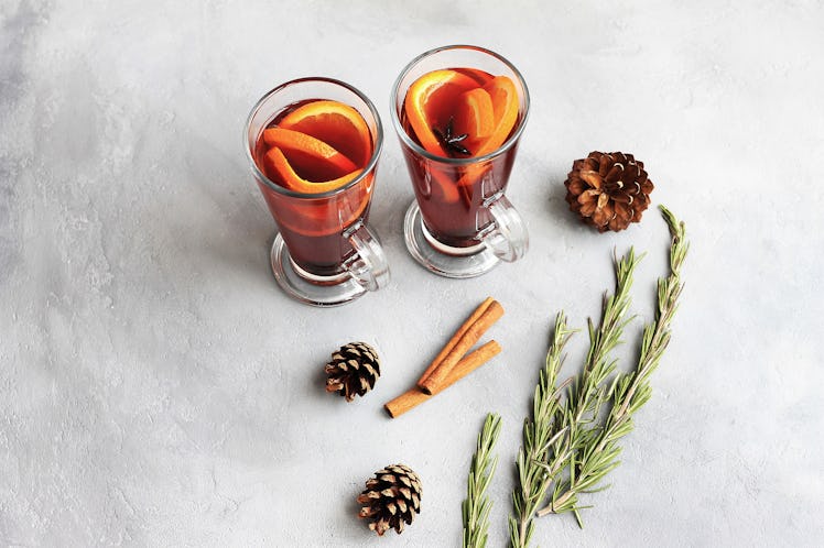 Two fall-inspired cocktails sit on a concrete table with cinnamon sticks and pinecones, which you co...