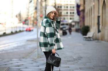 A young woman in a flannel-printed shacket walks down a city street.
