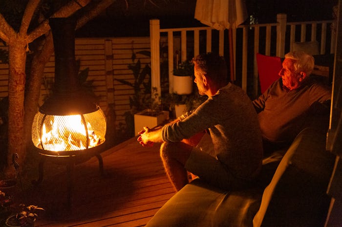 two men sitting outside in front of outdoor heater