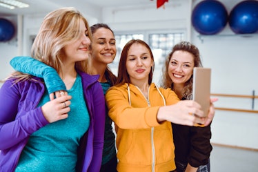 A group of women take a selfie on their phone while wearing brightly-colored sweatshirts.