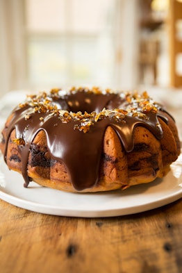 A pumpkin spice cake sits on a wooden counter and has a chocolate frosting on top.