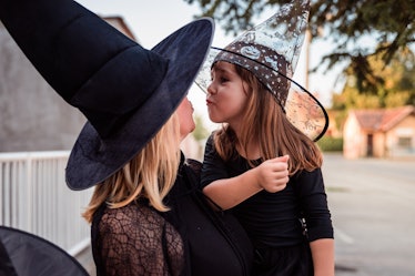 A blonde woman dressed like a witch on Halloween kneels down while her niece who's also dressed like...