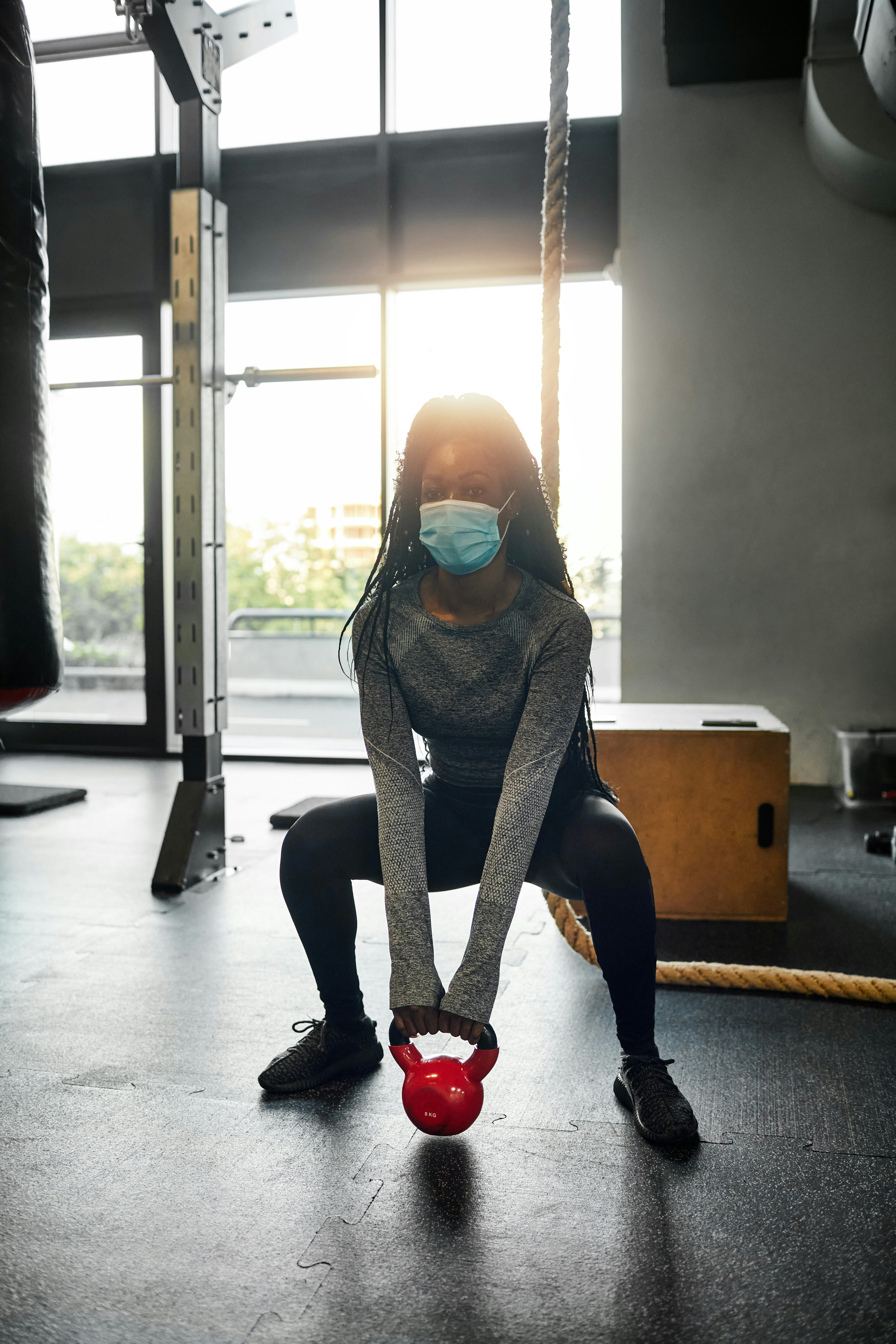 A person wearing a mask performs a sumo kettlebell squat in the gym