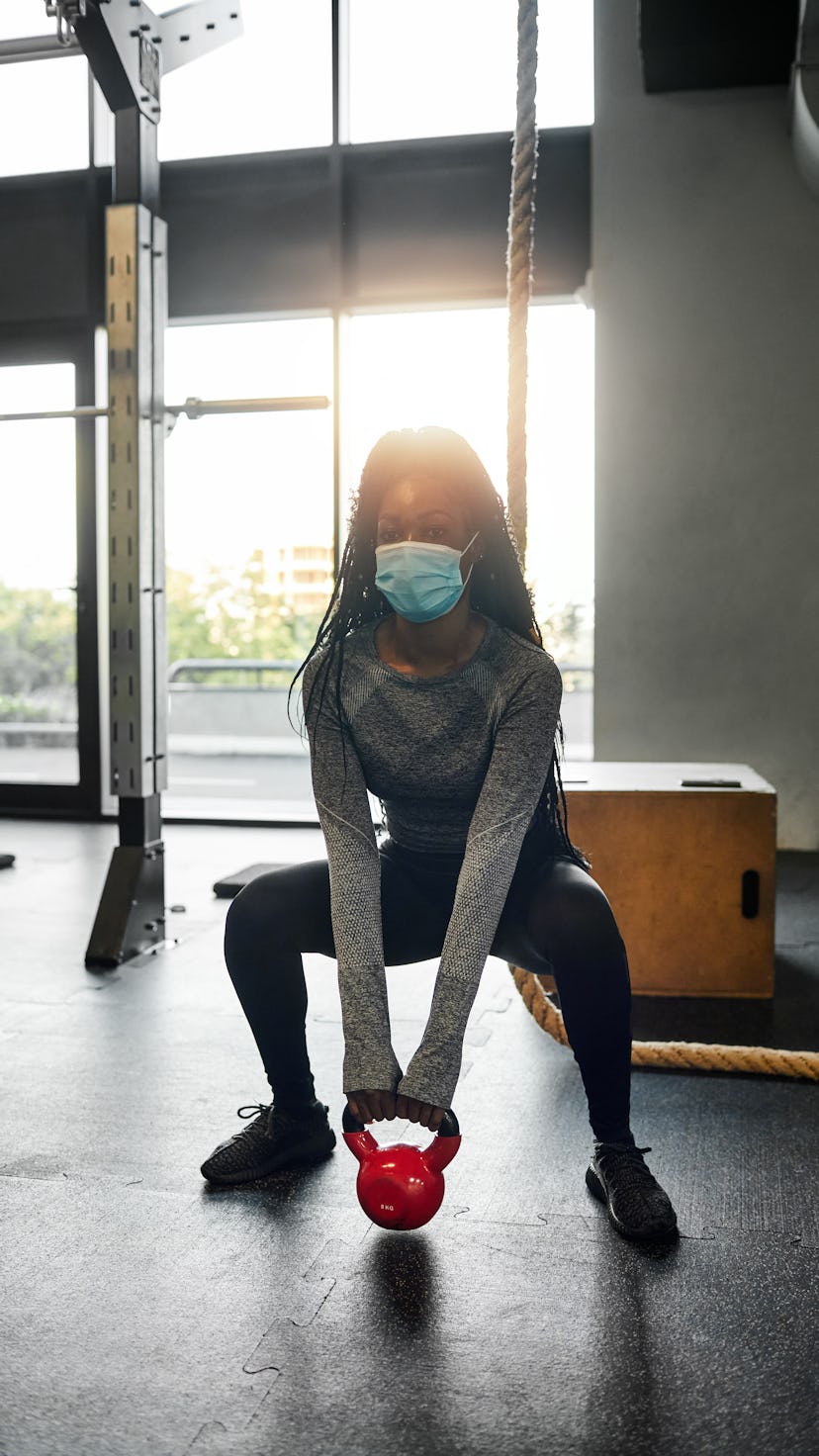 A person wearing a mask performs a sumo kettlebell squat in the gym