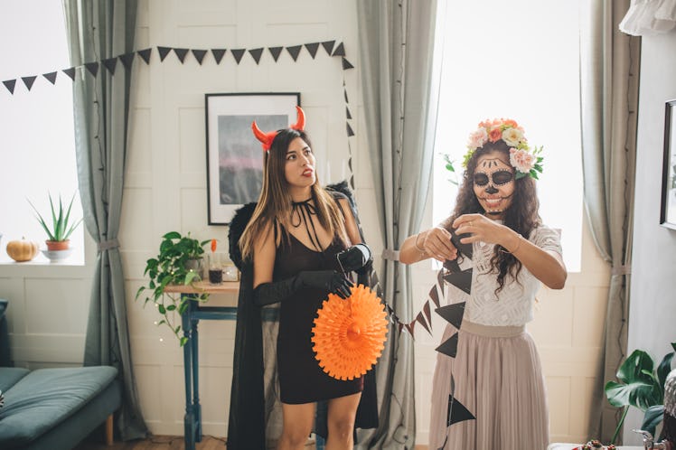 Two women hang up Halloween decorations in their home.
