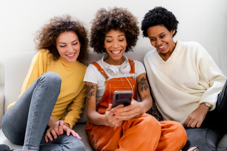 A group of happy women huddle together to look at a phone.