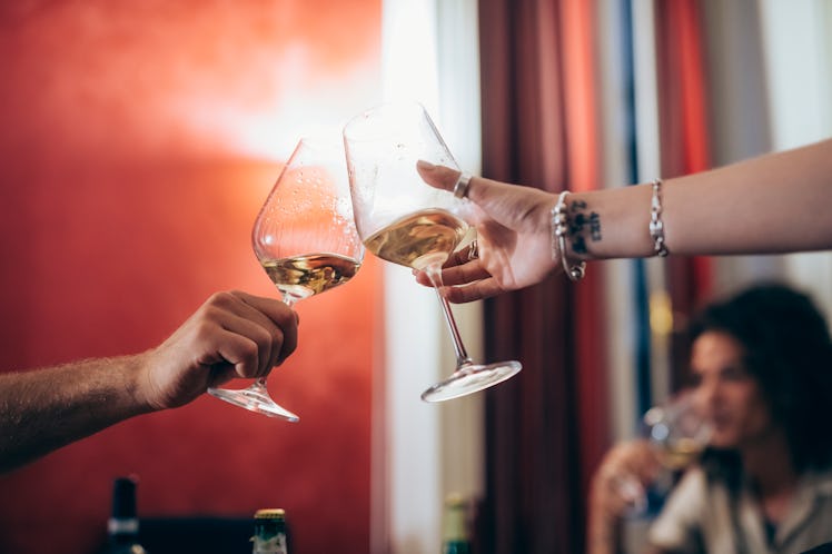 A young couple holds up glasses of white wine and clinks them together.