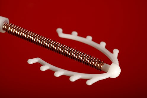 A copper IUD against a red background. IUDs can have many side effects, including bleeding and cramp...
