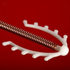 A copper IUD against a red background. IUDs can have many side effects, including bleeding and cramp...