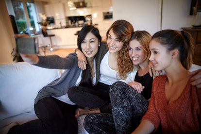 A group of women sitting on the couch at home, pose for a selfie. 