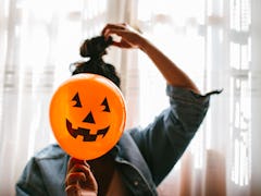 A young woman holds a pumpkin balloon in front of her face on Halloween.