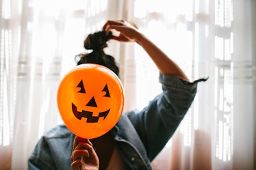 A young woman holds a pumpkin balloon in front of her face on Halloween.