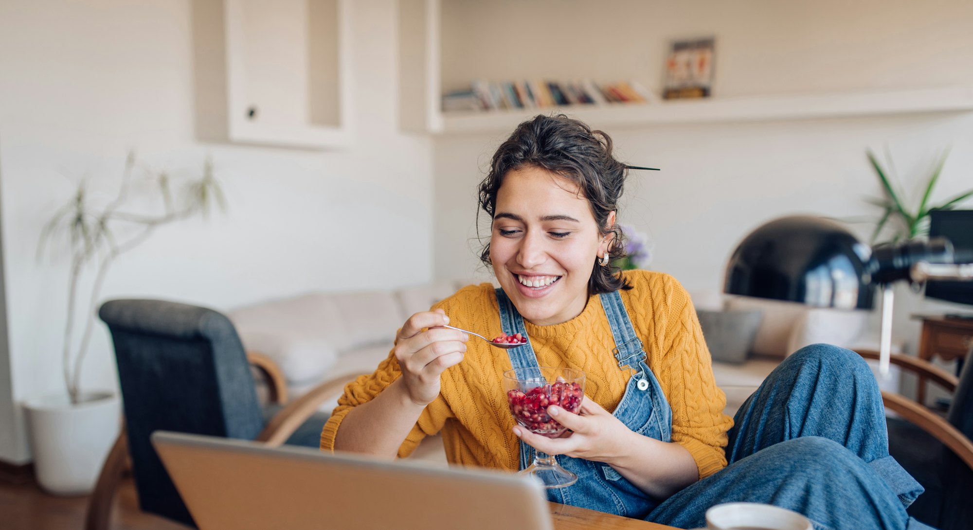 A woman eating a pomegranate with spoon during an online meeting