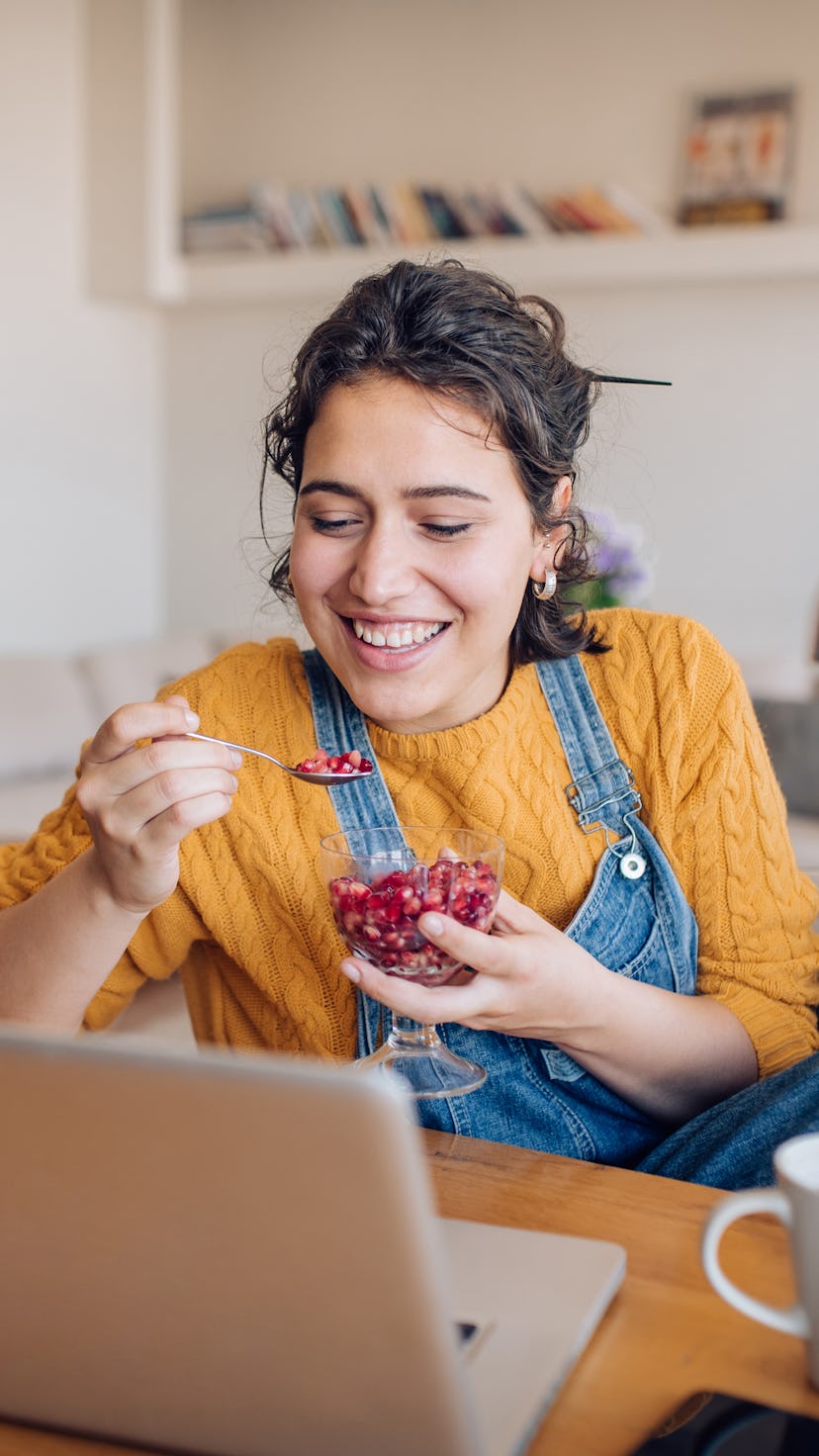 A woman eating a pomegranate with spoon during an online meeting