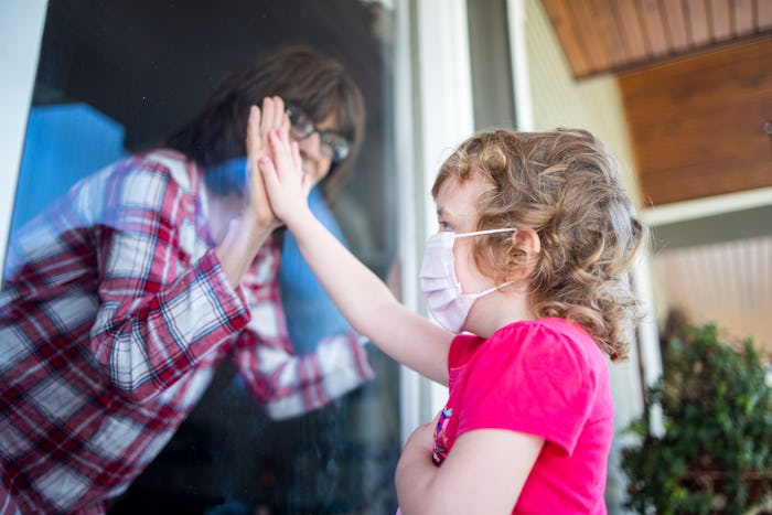 little boy greeting grandma through the window, both wear face masks