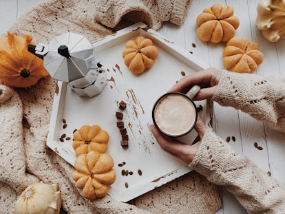A woman sets down a cup of pumpkin spice coffee on a tray filled with mini pumpkins. 