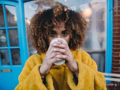 A woman in a yellow sweater enjoys a cup of coffee outside. 